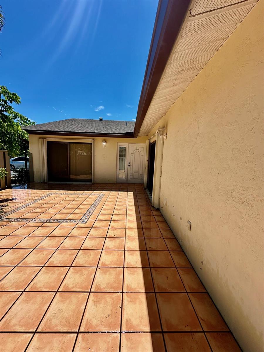A tiled patio area features a sliding glass door and a white exterior door — 8076 Ambach Way, Hypoluxo FL 33462, HYPOLUXO, FL