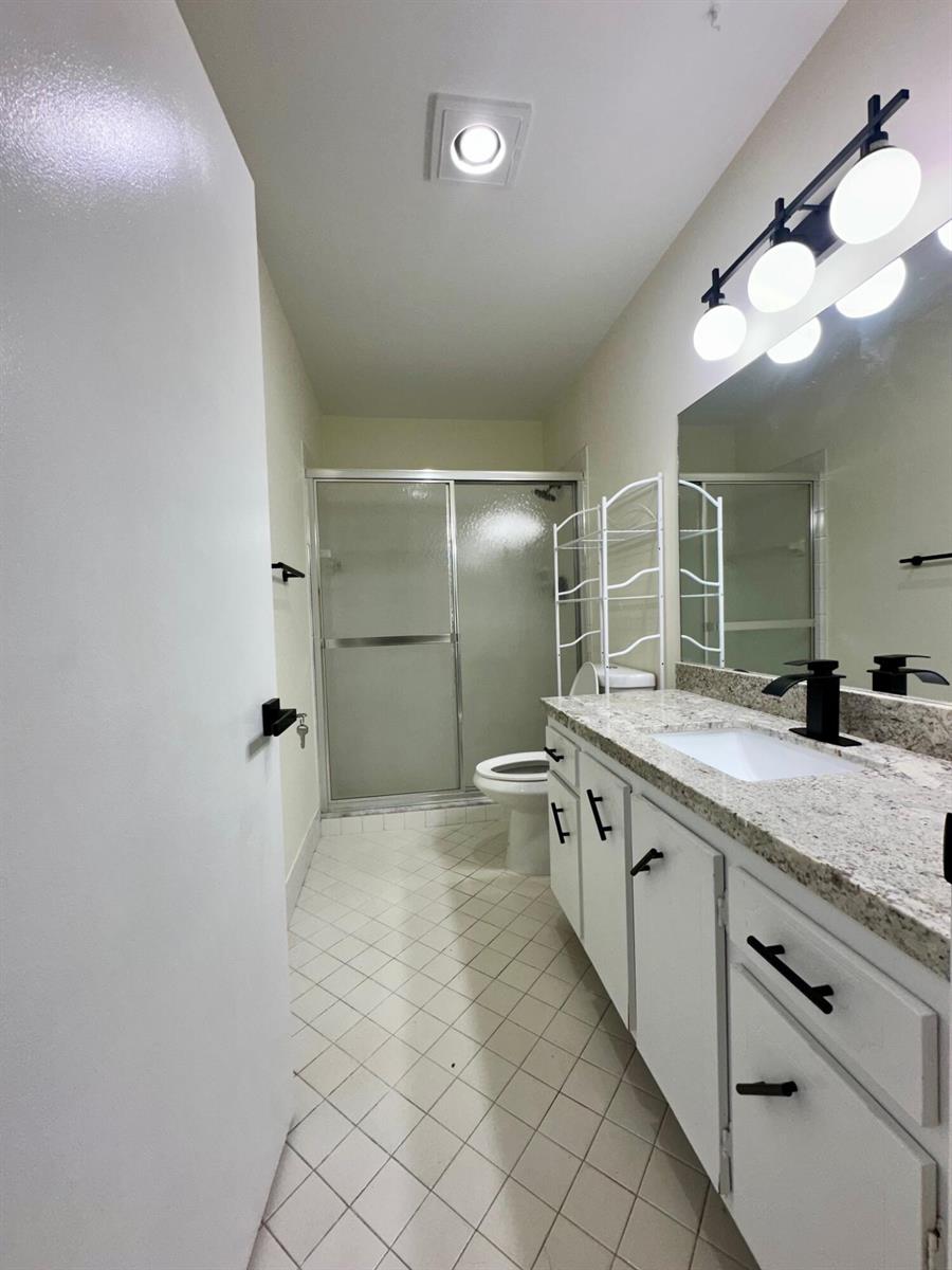 A bathroom features a granite vanity, white cabinets, a walk-in shower, and tile flooring — 8076 Ambach Way, Hypoluxo FL 33462, HYPOLUXO, FL