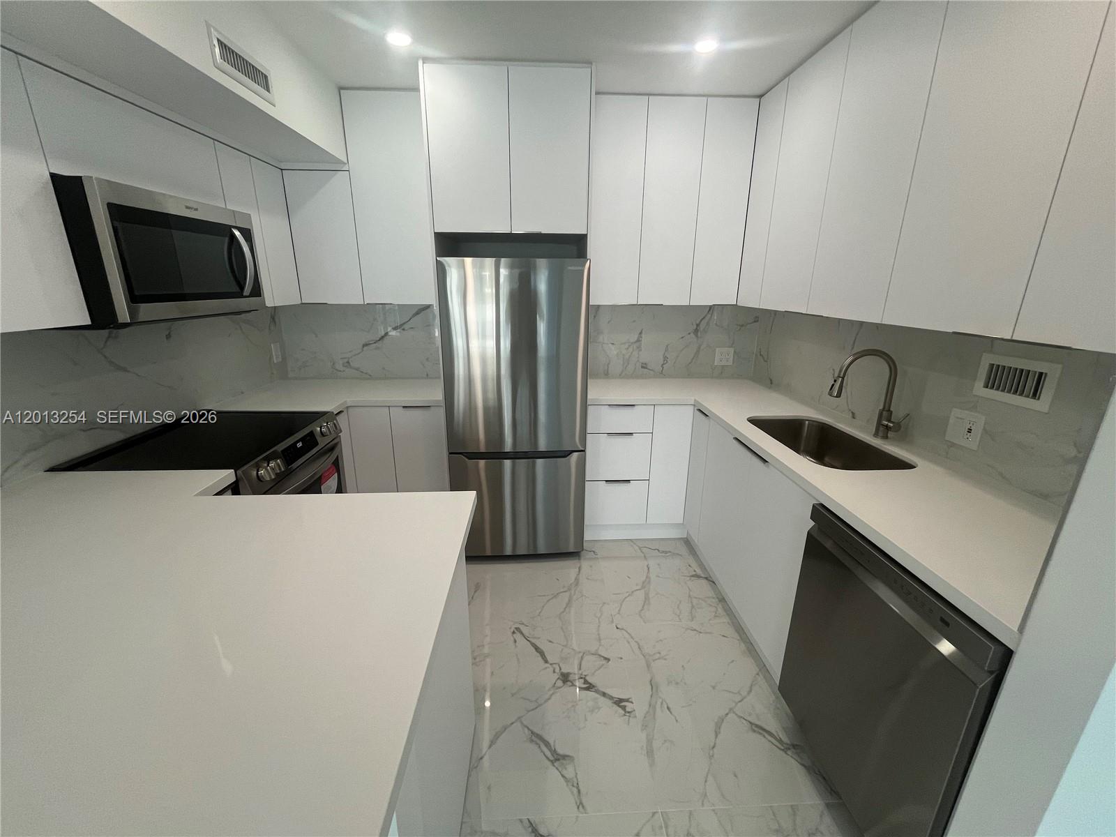 A modern kitchen features white flat-panel cabinets, stainless steel appliances, and marble-patterned countertops and flooring — 3505 S Ocean Dr # 210, Hollywood FL 33019, HOLLYWOOD, FL