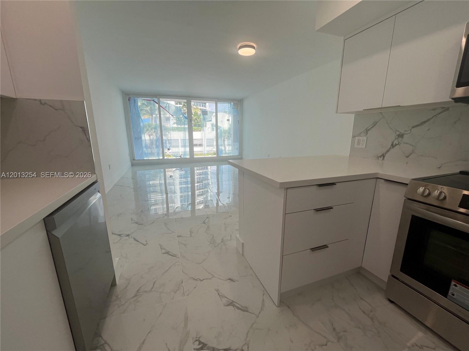 A modern kitchen with white cabinets and marble-style flooring opens to a living area — 3505 S Ocean Dr # 210, Hollywood FL 33019, HOLLYWOOD, FL