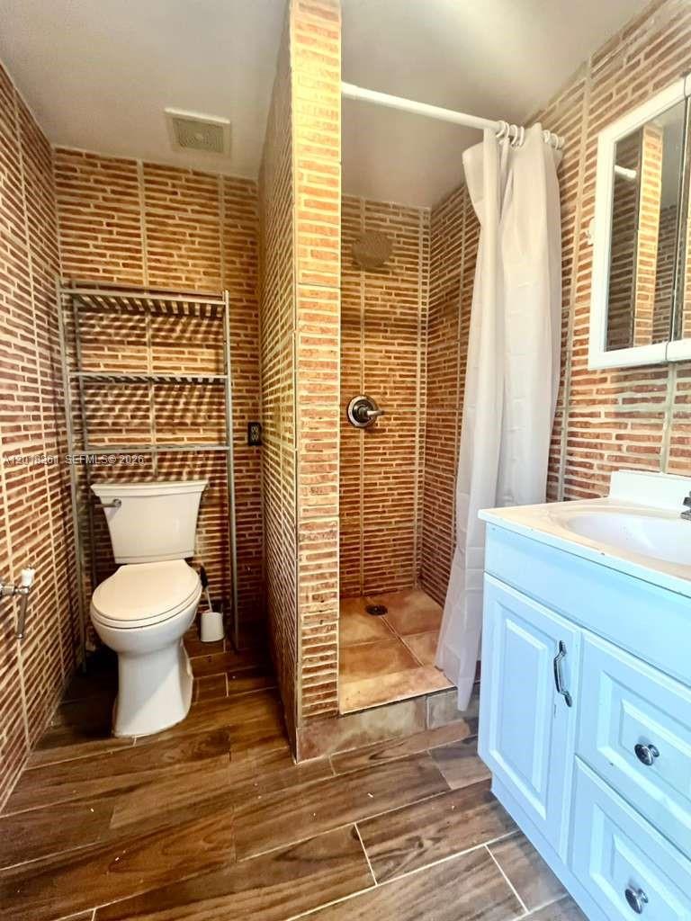 A bathroom features brick-tiled walls, a walk-in shower, a toilet with shelving, and a vanity — 1875 NE 177th St # 0, North Miami Beach FL 33162, NORTH MIAMI BEACH, FL