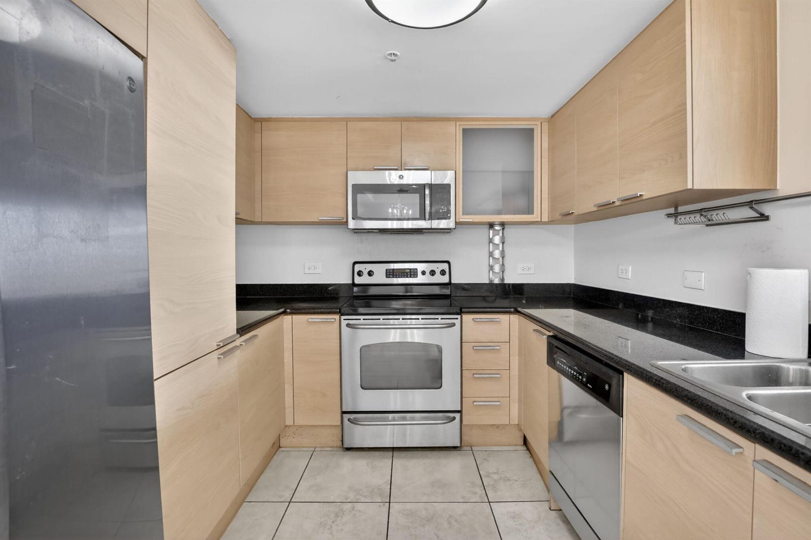 A galley kitchen features light wood cabinets, stainless steel appliances, and black granite countertops — 140 S Dixie Highway # 819, Hollywood FL 33020, HOLLYWOOD, FL