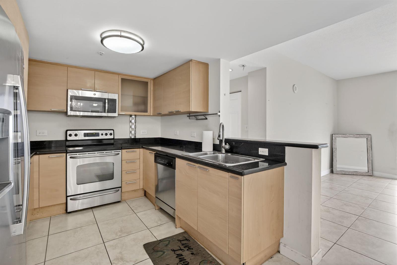 A kitchen features light wood cabinets, black countertops, stainless steel appliances, and tiled flooring — 140 S Dixie Highway # 819, Hollywood FL 33020, HOLLYWOOD, FL