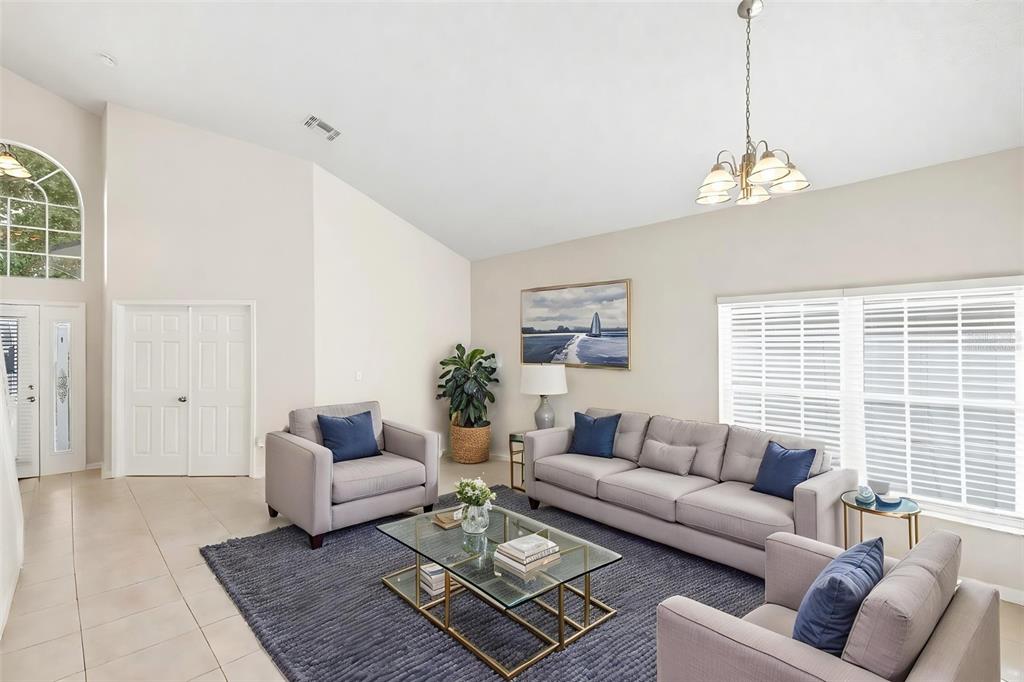 A living room with a vaulted ceiling, gray sofa set, glass coffee table, and rug — 7946 GOLDEN POND CIRCLE, KISSIMMEE, FL