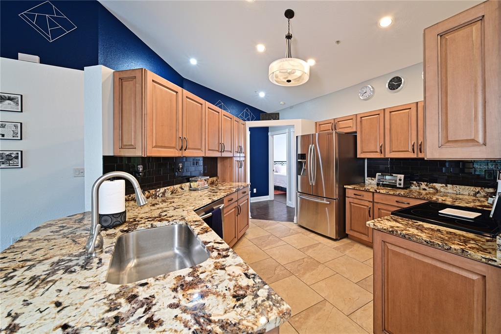A kitchen features wood cabinets, granite countertops, stainless steel appliances, and a dark blue wall — 6589 FAIRWAY GARDENS DRIVE UNIT 202, BRADENTON, FL