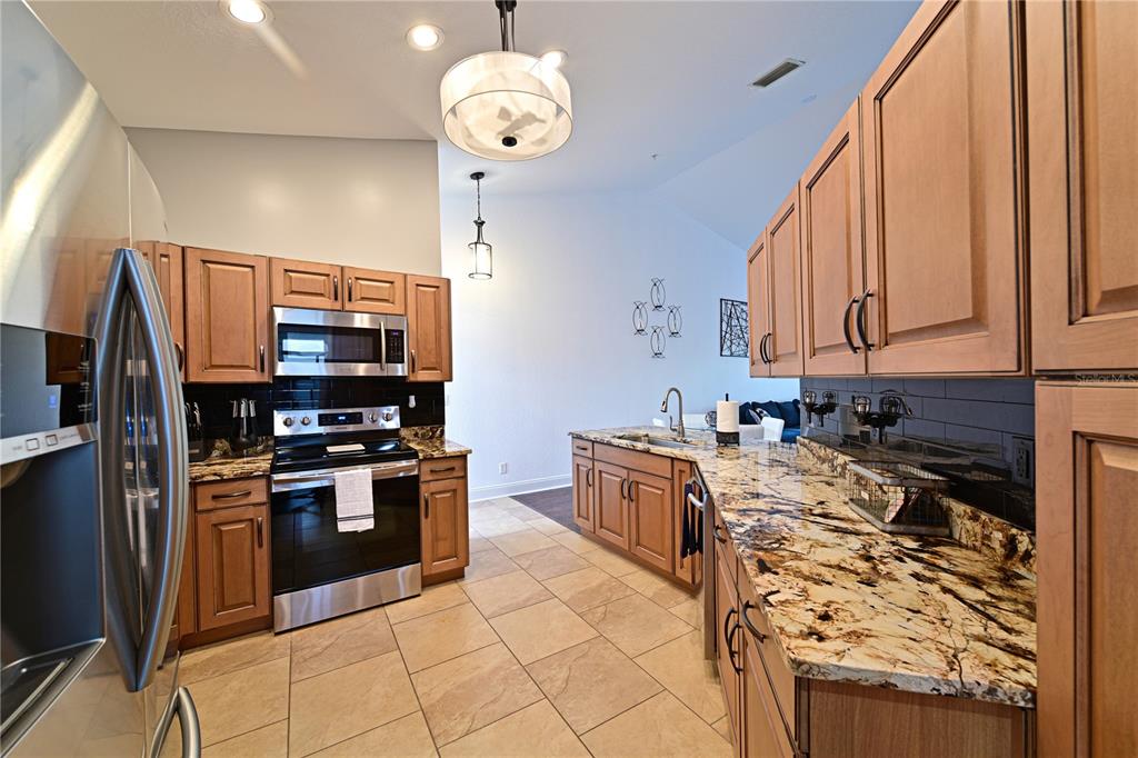 A kitchen features wood cabinets, granite countertops, stainless steel appliances, and tile flooring — 6589 FAIRWAY GARDENS DRIVE UNIT 202, BRADENTON, FL