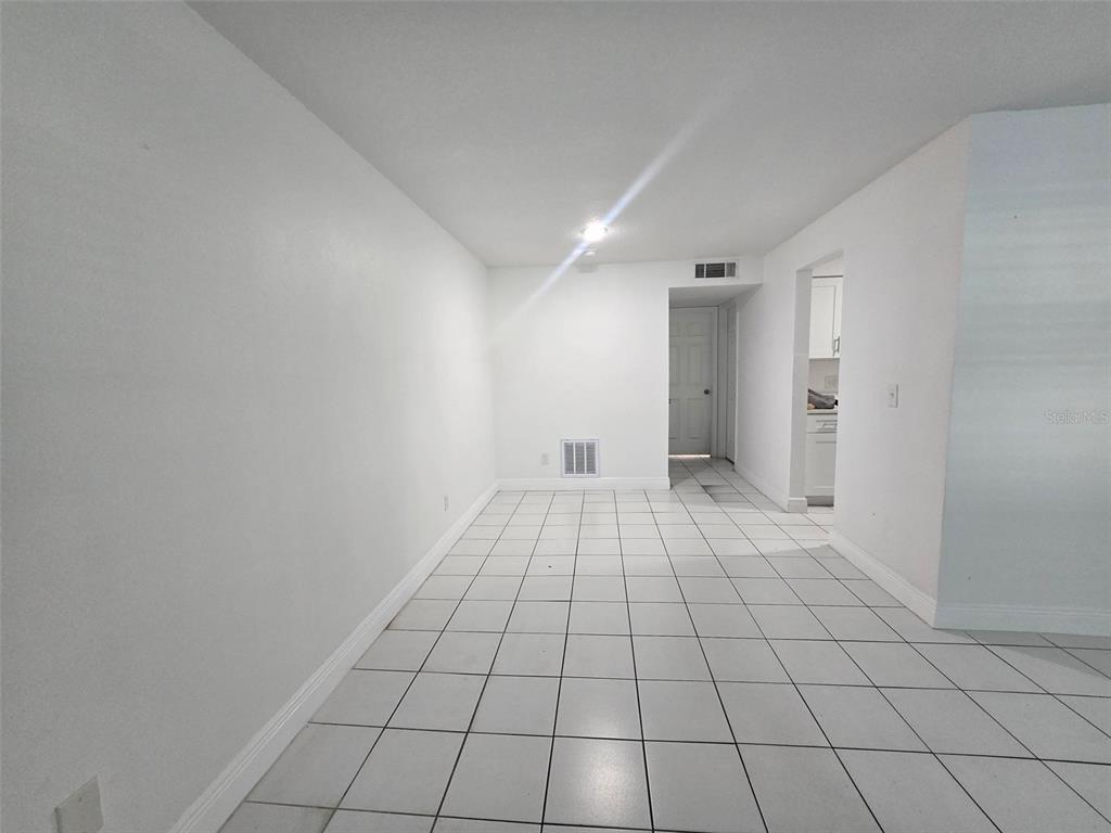 A room with white walls and white tiled flooring leads to a doorway and kitchen — 9009 TUDOR DRIVE UNIT G107, TAMPA, FL