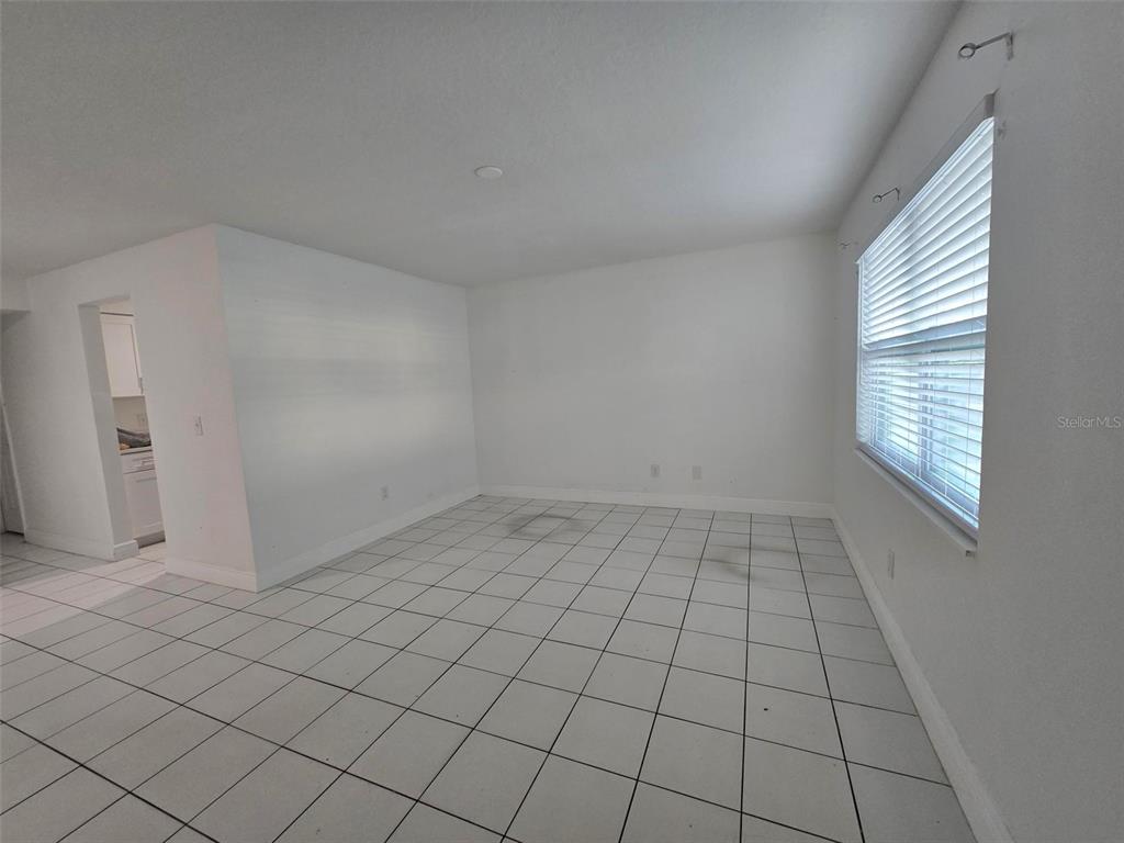 An empty room features white walls, white tile flooring, and a window with blinds — 9009 TUDOR DRIVE UNIT G107, TAMPA, FL