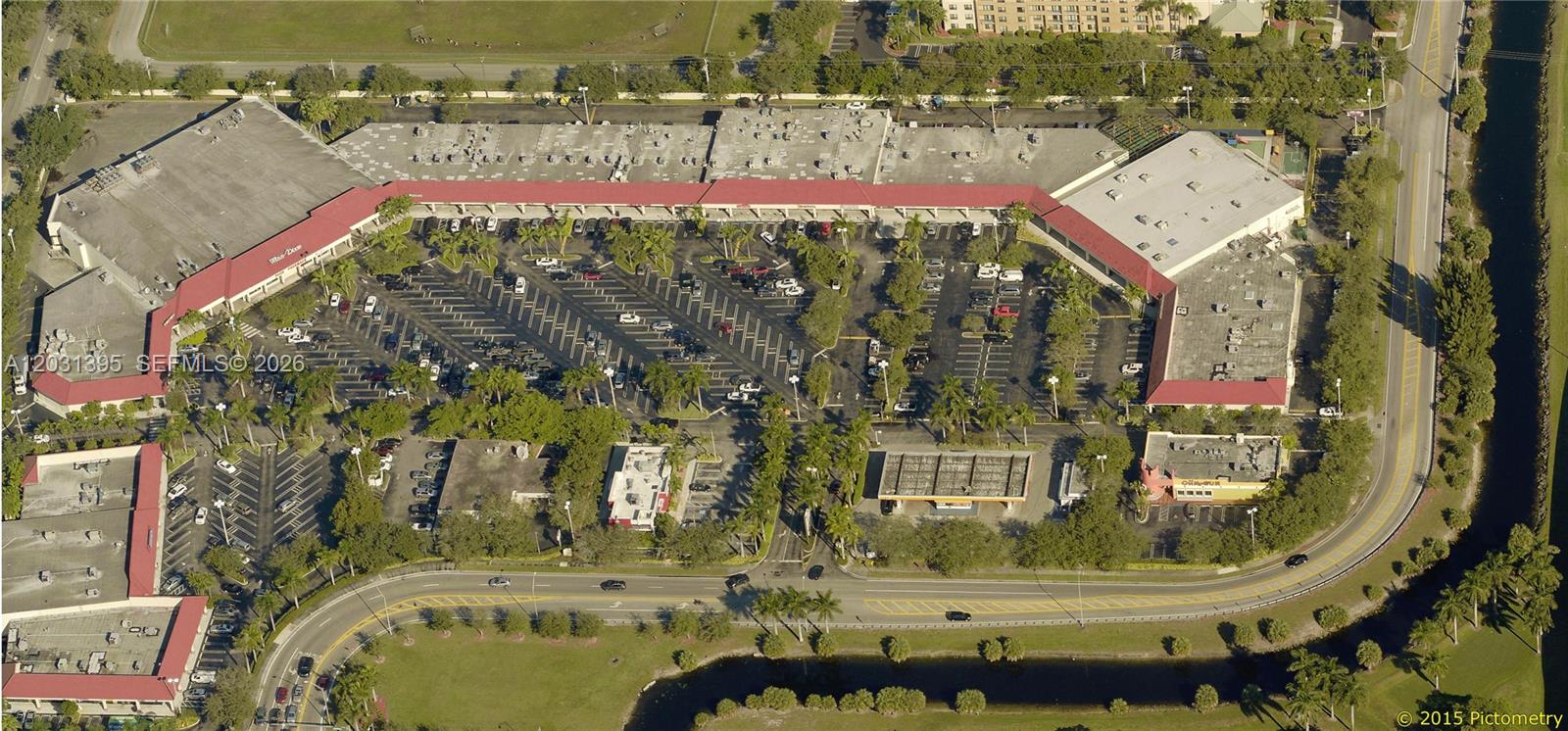 An aerial view shows a commercial shopping center with a large parking lot and landscaping — MIAMI LAKES, FL