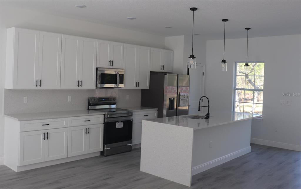 A modern kitchen features white cabinetry, stainless steel appliances, and a quartz-topped island — 3717 W MALBY LANE, CITRUS SPRINGS, FL