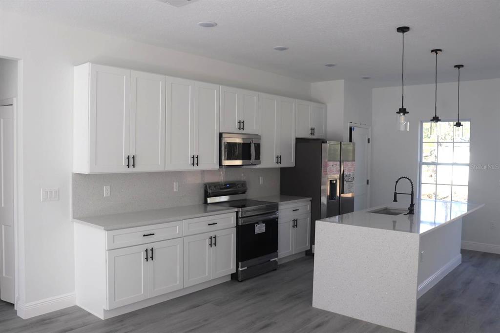A modern kitchen features white cabinetry, stainless steel appliances, and a quartz-topped island — 3717 W MALBY LANE, CITRUS SPRINGS, FL