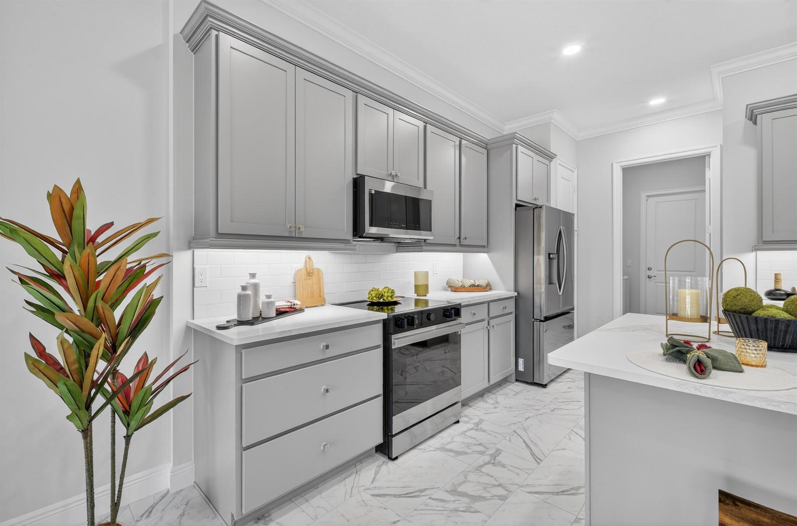 A modern kitchen features gray cabinets, stainless steel appliances, white countertops, and marble-patterned tile flooring — 1805 Bridgepointe Circle # 2, Vero Beach FL 32967, VERO BEACH, FL