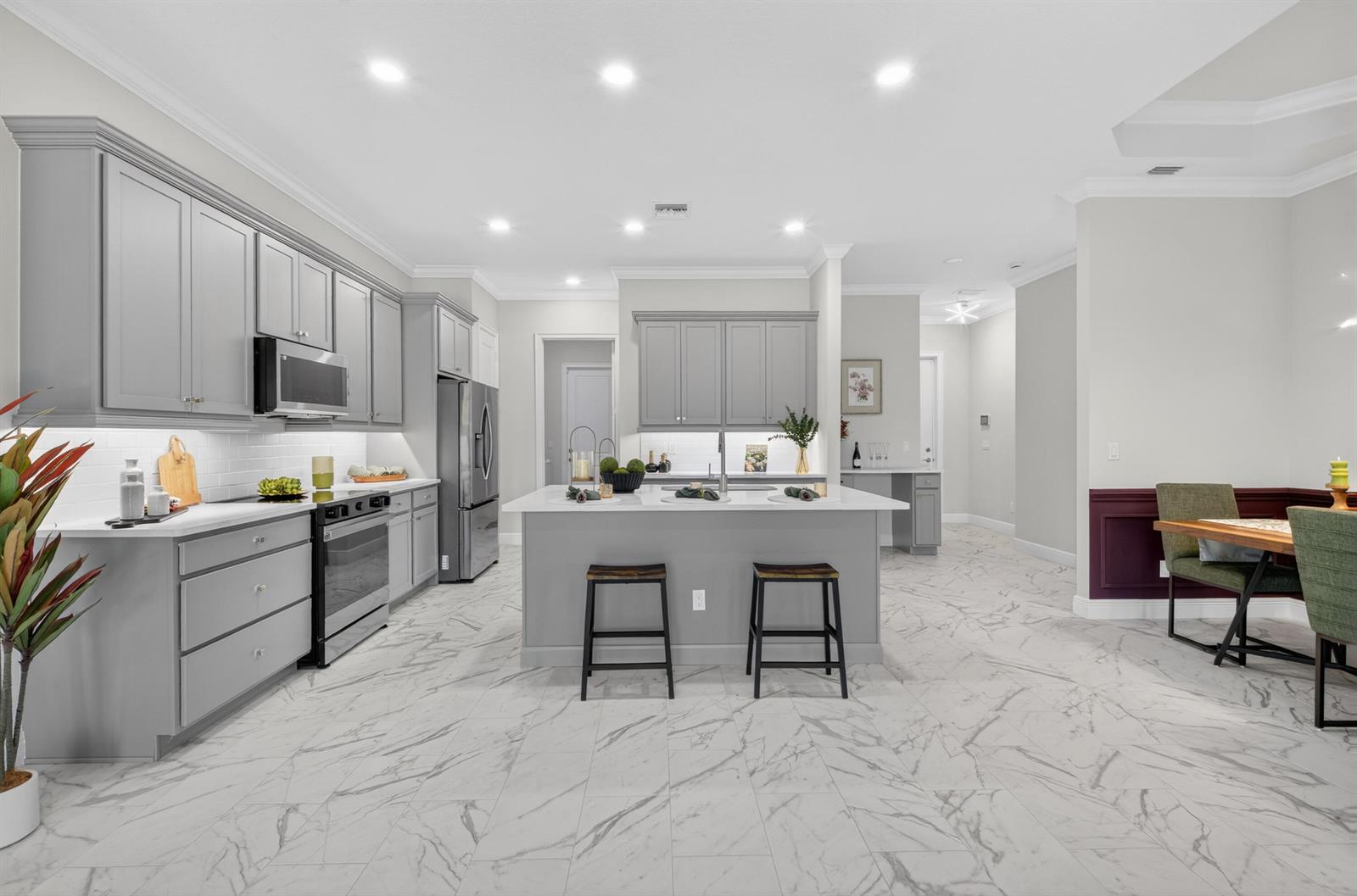 A modern kitchen features grey cabinetry, a central island with bar stools, and marble-patterned flooring — 1805 Bridgepointe Circle # 2, Vero Beach FL 32967, VERO BEACH, FL