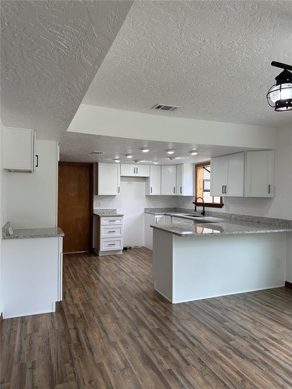 A kitchen features white cabinets, granite countertops, and wood-look flooring — 2598 ENTERPRISE OSTEEN ROAD, OSTEEN, FL