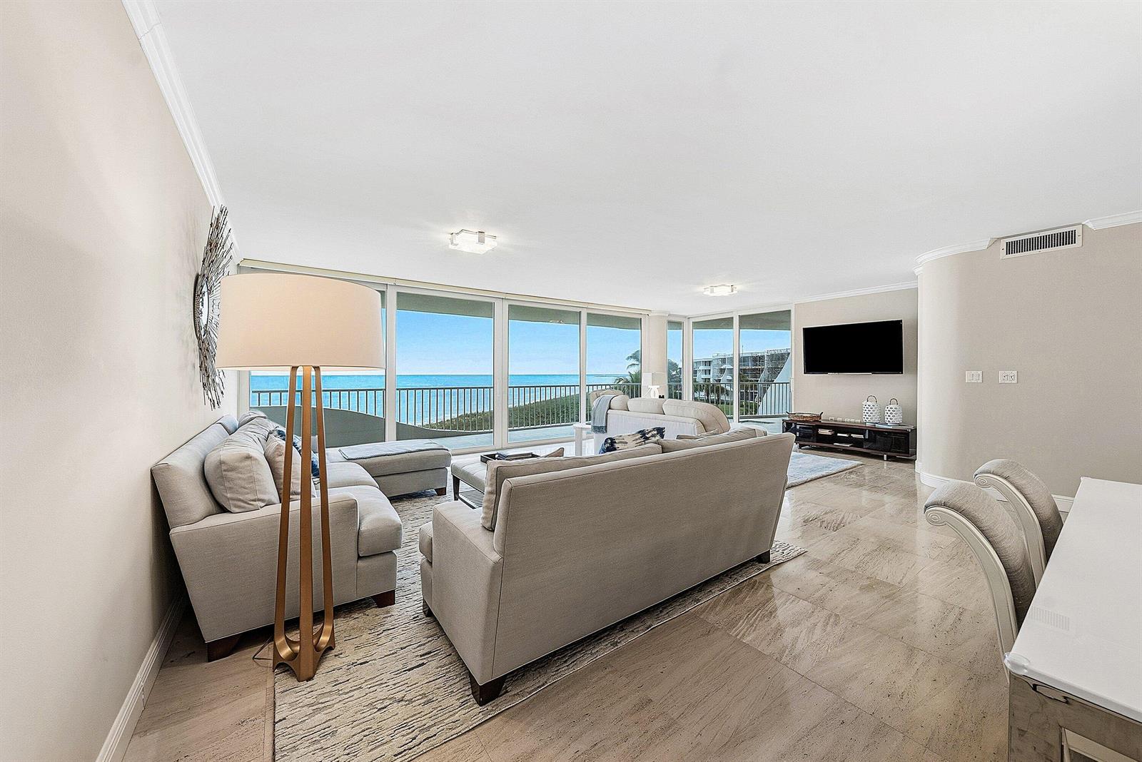 A living room features light-colored sofas, a floor lamp, and large windows overlooking the ocean — 2001 SE Sailfish Point Boulevard # 313, Stuart FL 34996, STUART, FL
