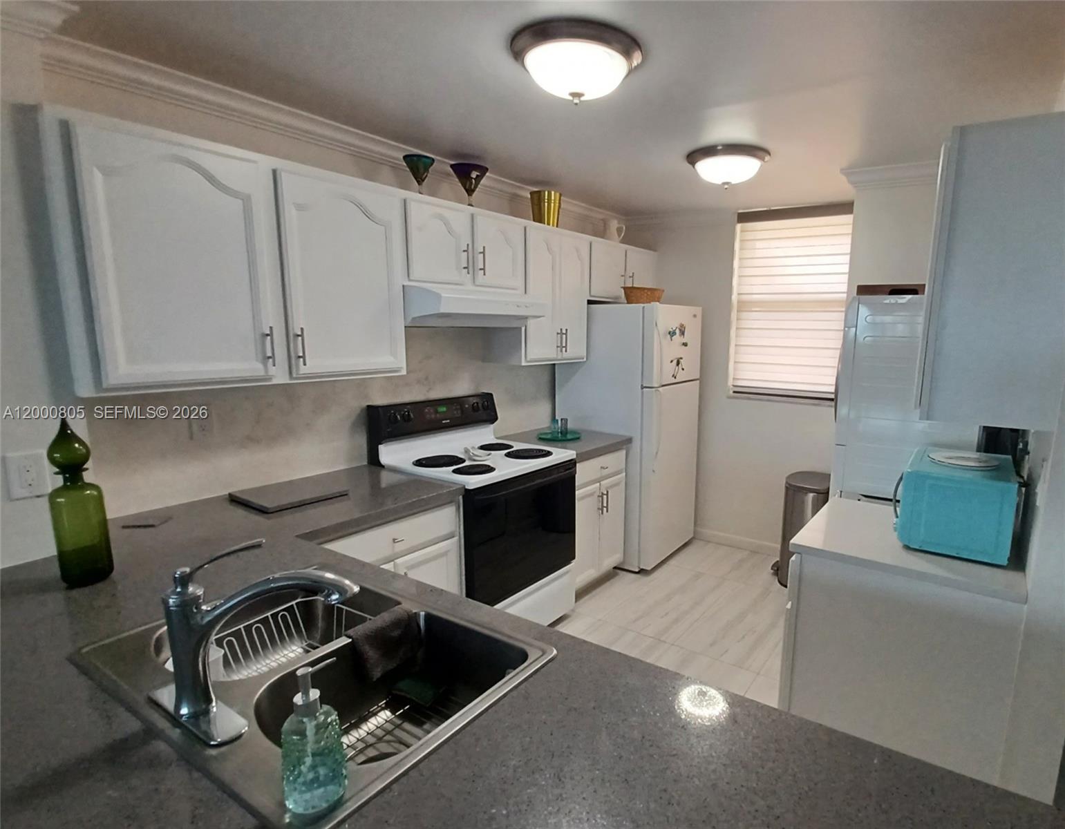 A kitchen features white cabinets, gray countertops, stainless steel appliances, and a double-basin sink — 9900 S Ocean Dr # 106, Jensen Beach FL 34957, JENSEN BEACH, FL