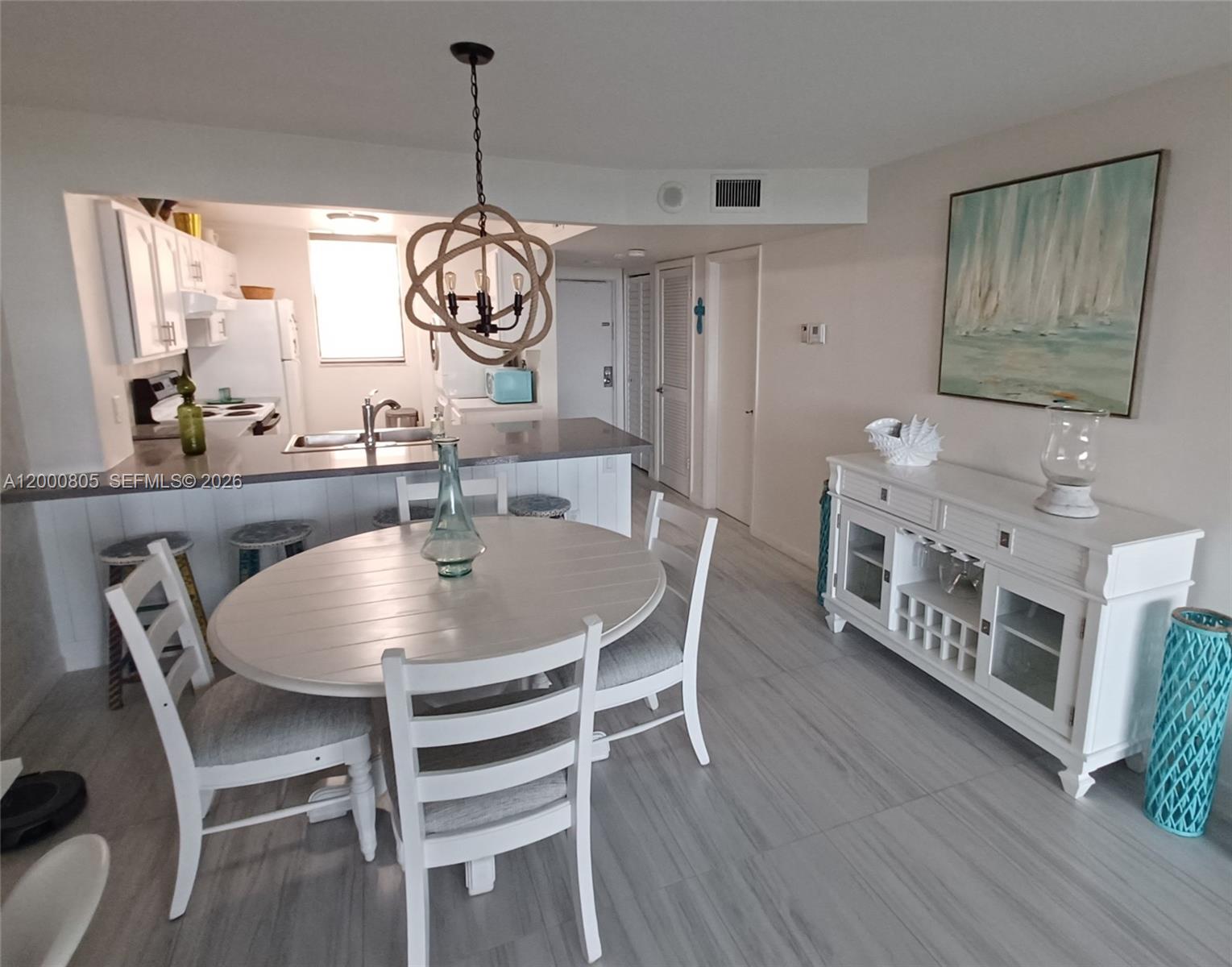 A dining area with a round table, white chairs, and a sideboard sits near a kitchen — 9900 S Ocean Dr # 106, Jensen Beach FL 34957, JENSEN BEACH, FL