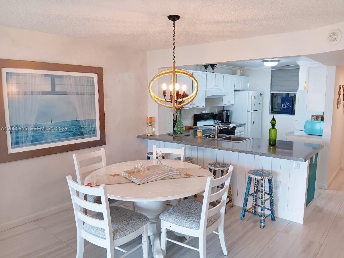 A dining area with a round table and pendant light opens into a white kitchen — 9900 S Ocean Dr # 106, Jensen Beach FL 34957, JENSEN BEACH, FL