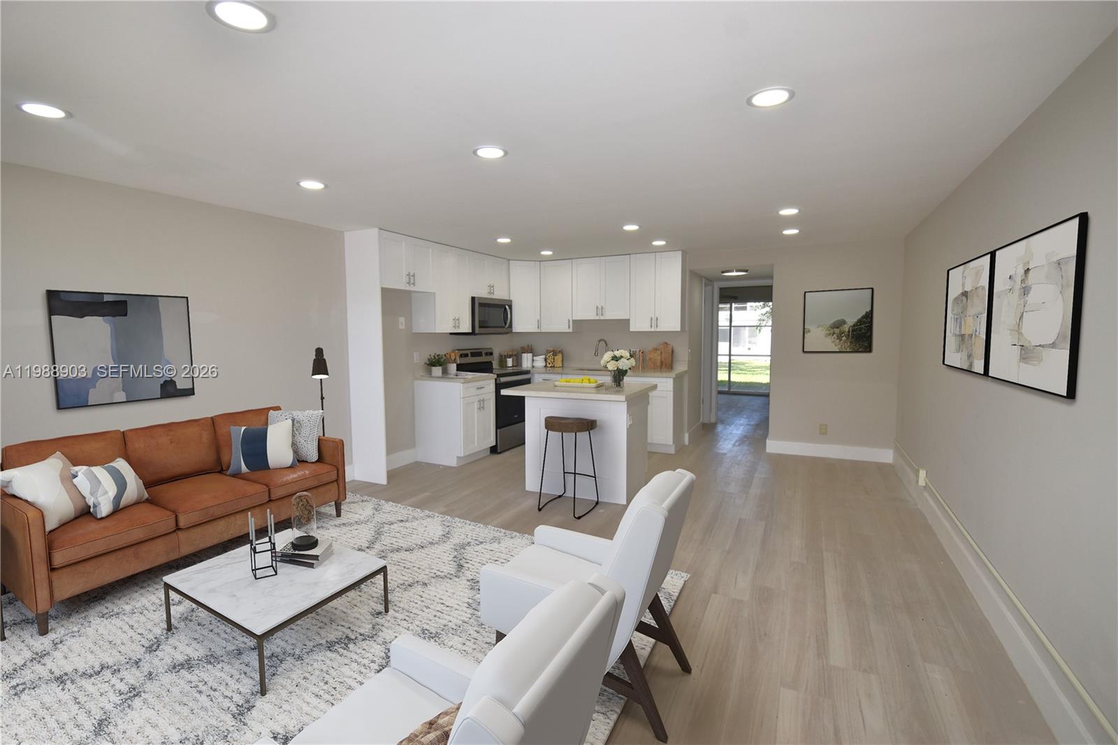 An open-concept living room and kitchen feature white cabinetry, light wood flooring, and modern furniture — 152 Ventnor J # 152, Deerfield Beach FL 33442, DEERFIELD BEACH, FL