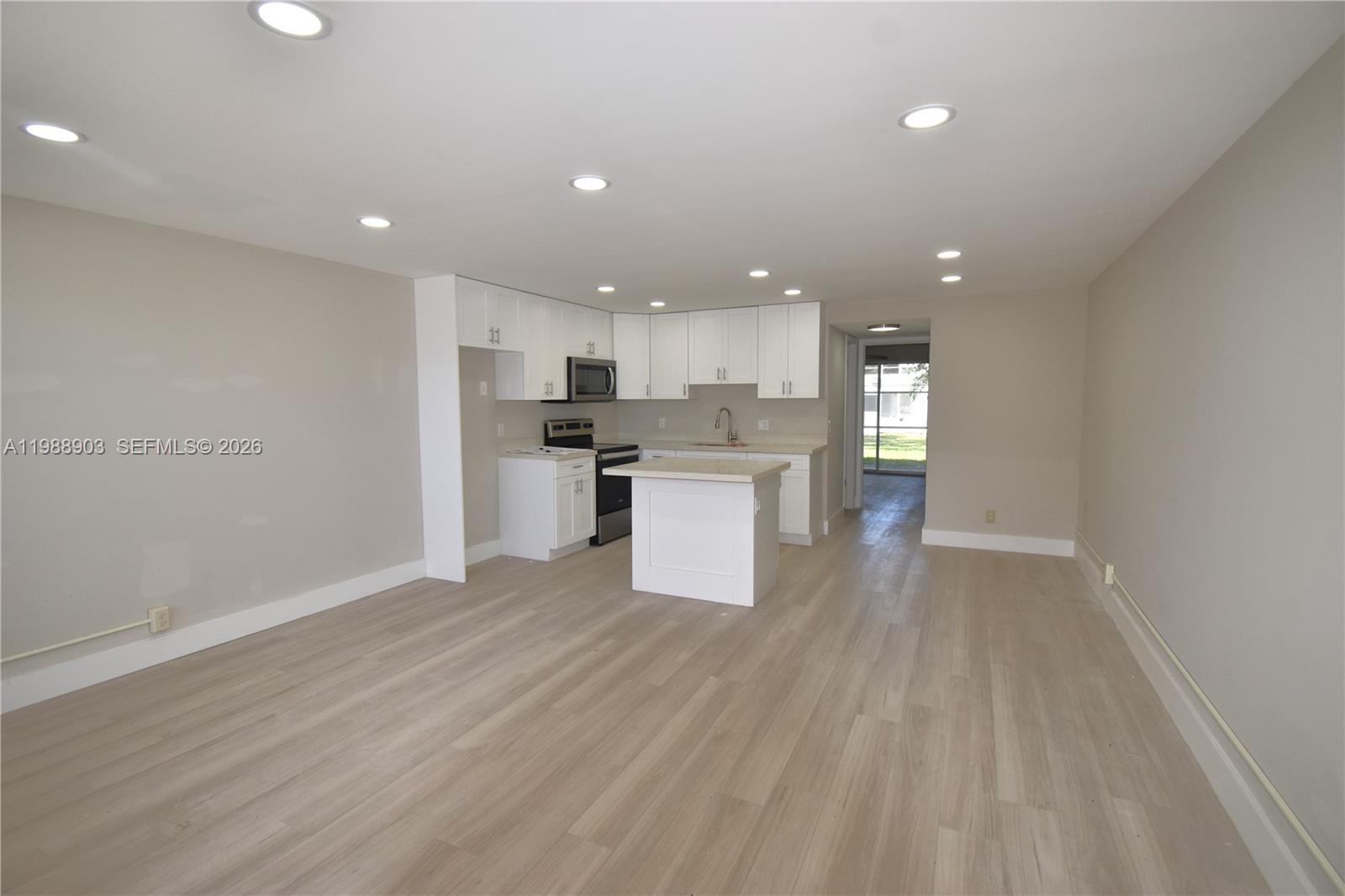 A kitchen with white cabinets and a center island opens into a living area — 152 Ventnor J # 152, Deerfield Beach FL 33442, DEERFIELD BEACH, FL