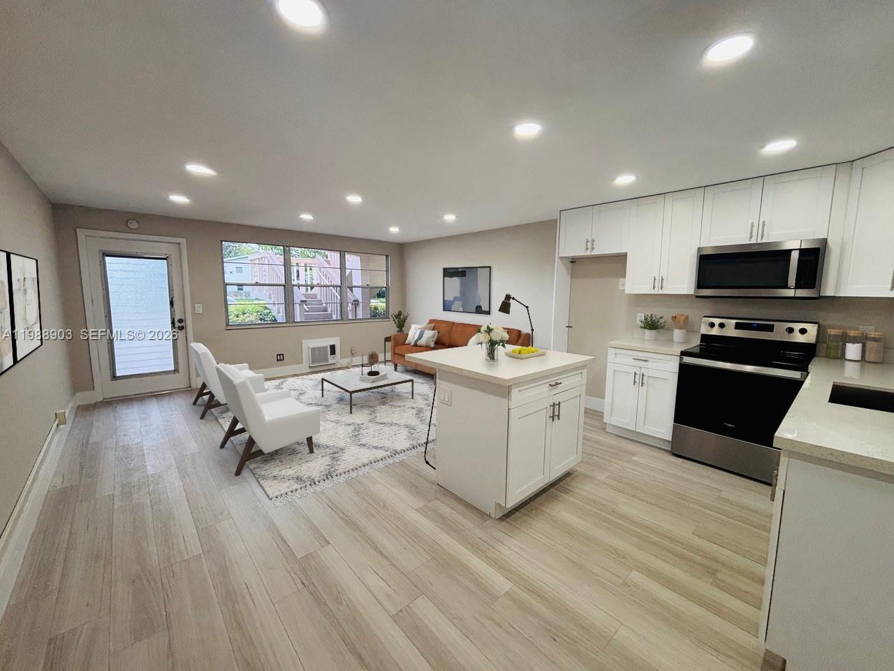 An open-concept kitchen and living area features white cabinetry, stainless steel appliances, and wood-look flooring — 152 Ventnor J # 152, Deerfield Beach FL 33442, DEERFIELD BEACH, FL