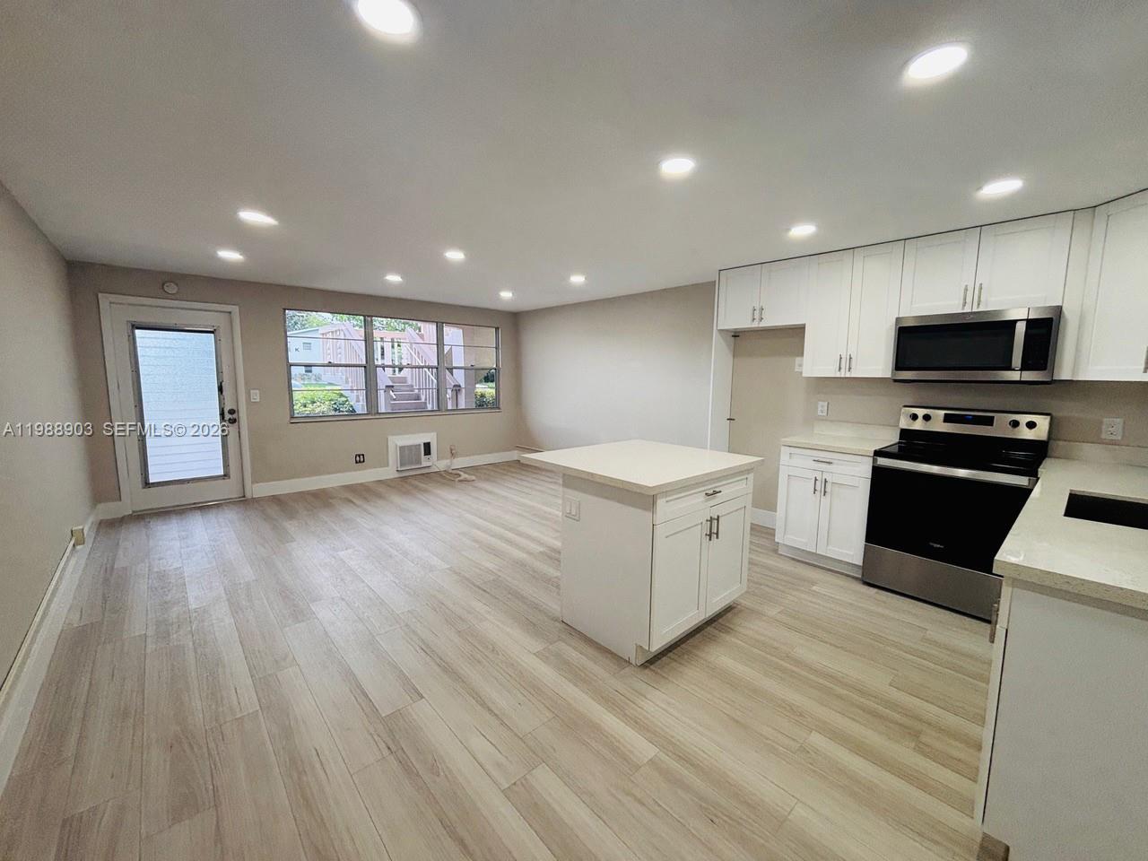 A kitchen and living area feature white cabinets, a center island, and light wood flooring — 152 Ventnor J # 152, Deerfield Beach FL 33442, DEERFIELD BEACH, FL