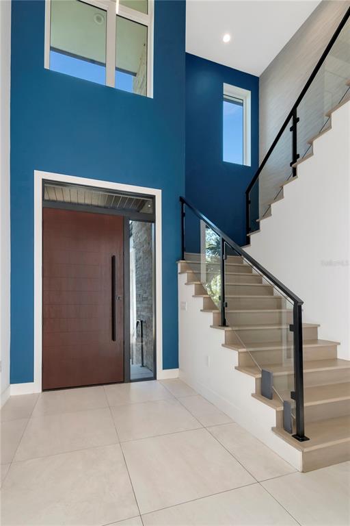 A modern entryway features a tall blue wall, a large wooden door, and a glass-railed staircase — 4604 W LOWELL AVENUE, TAMPA, FL