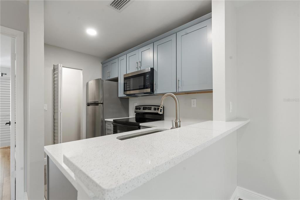 A kitchen features light blue cabinets, stainless steel appliances, and a white quartz breakfast bar — 3848 N LAKE DRIVE UNIT 138, TAMPA, FL