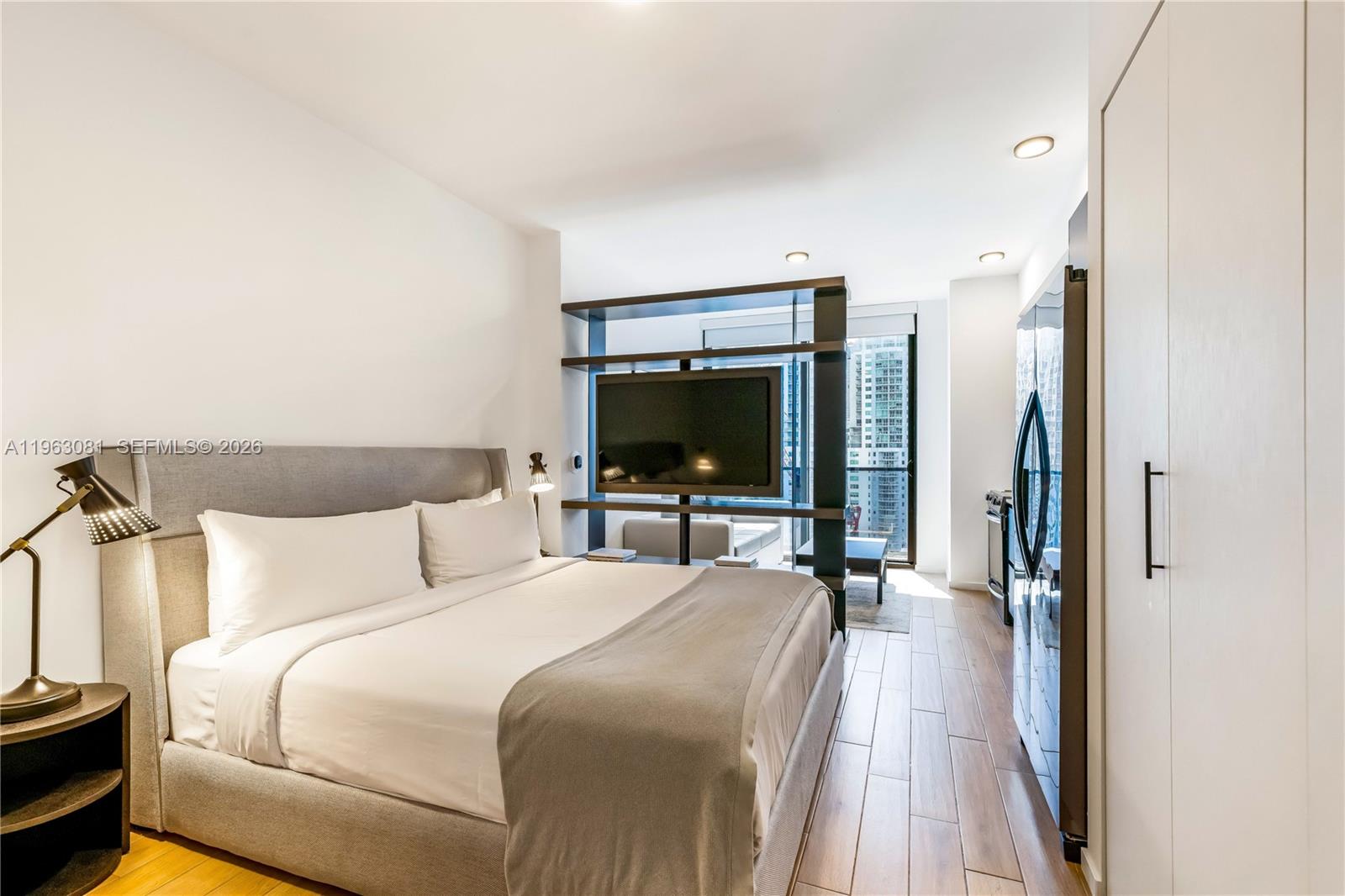 A studio bedroom features a bed, a room-dividing shelving unit with a television, and wood-look flooring — 398 NE 5th St # 2116, Miami FL 33132, MIAMI, FL