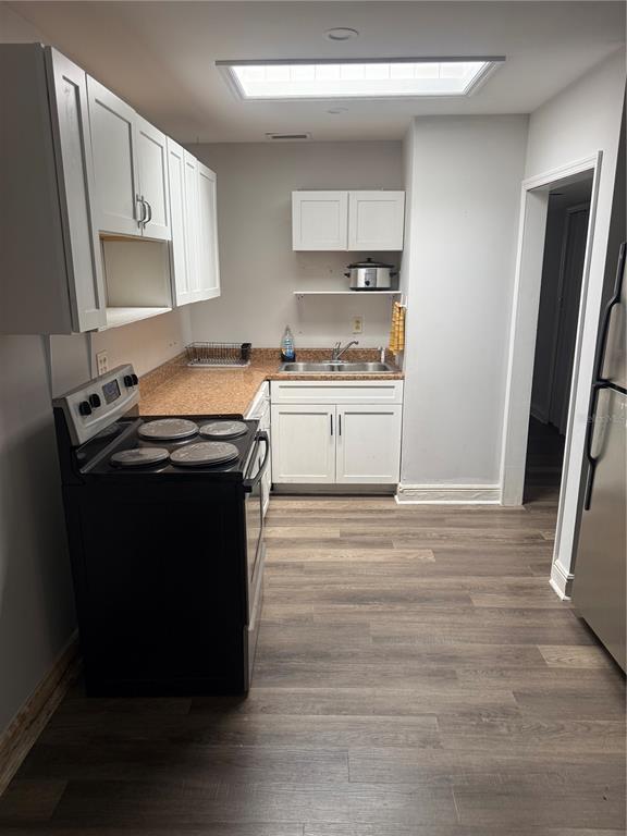 A kitchen features white cabinets, a black stove, a sink, and wood-look flooring — 500 E 25TH STREET, SANFORD, FL