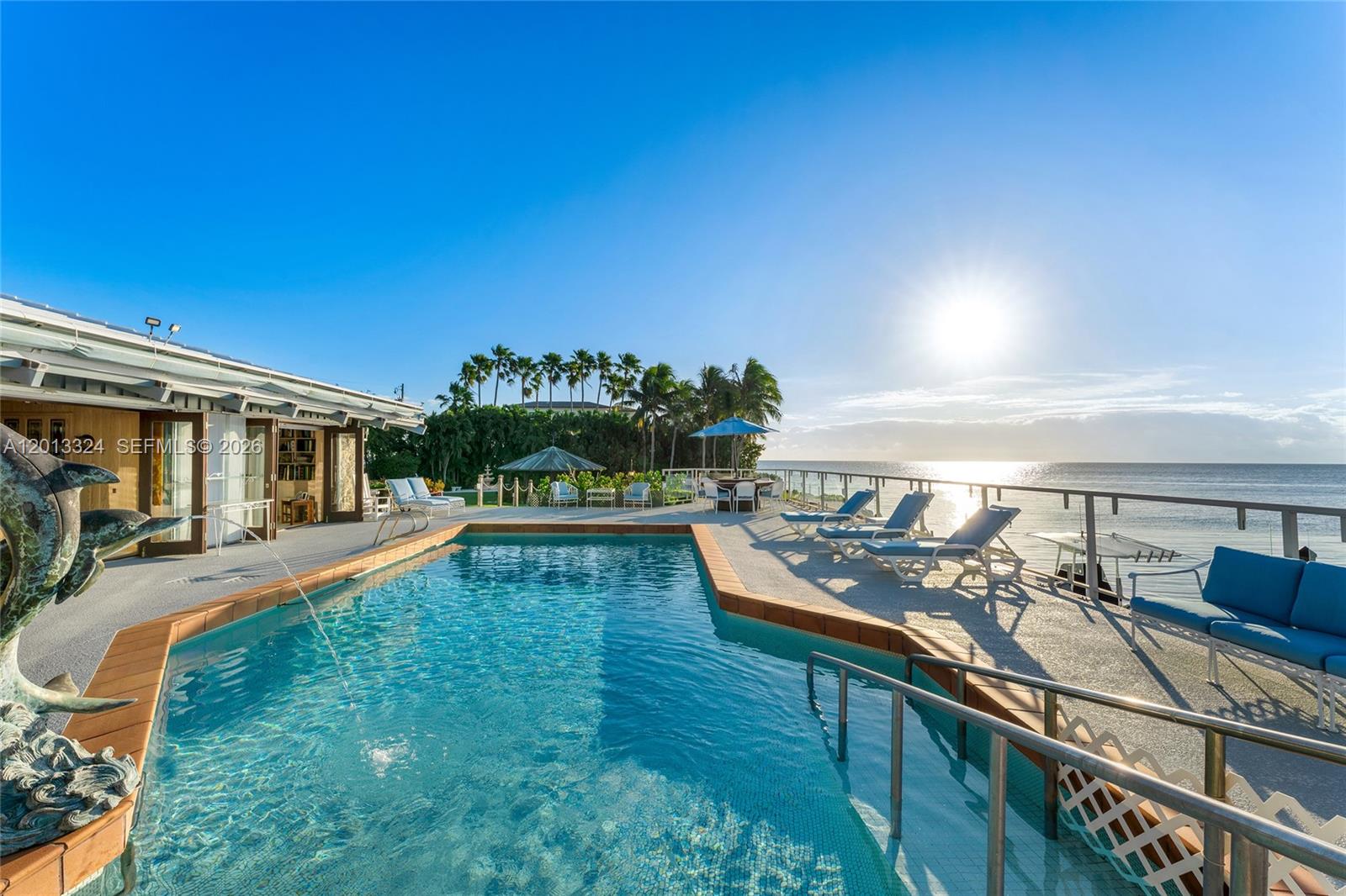 A swimming pool sits on a patio overlooking the ocean at sunset — 720 Lugo Ave, Coral Gables FL 33156, CORAL GABLES, FL