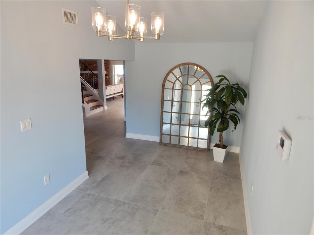 A light blue room features gray tile flooring, a chandelier, and a large arched mirror — 8025 ISLAND DRIVE, PORT RICHEY, FL
