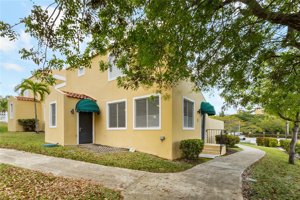A two-story yellow stucco building with green awnings and white-framed windows sits along a sidewalk — 215 HARBOUR DRIVE UNIT J1, HUMACAO, PR