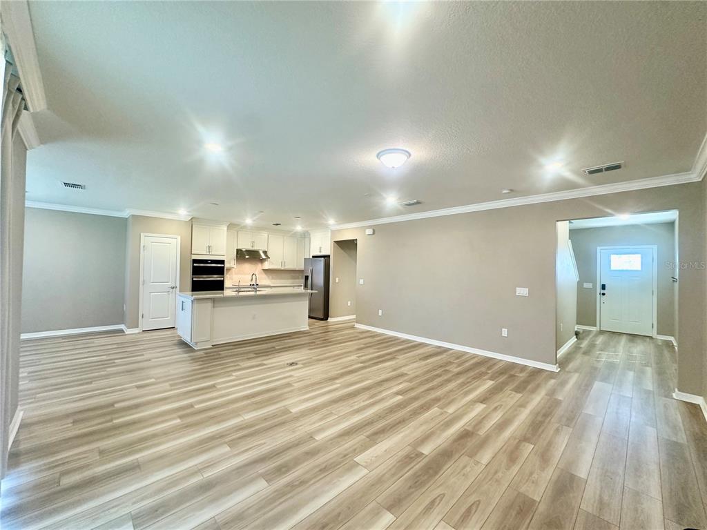 An open-concept kitchen and living area featuring light wood-look flooring and white cabinetry — 1066 SILVERLAKE BOULEVARD, LAKE ALFRED, FL