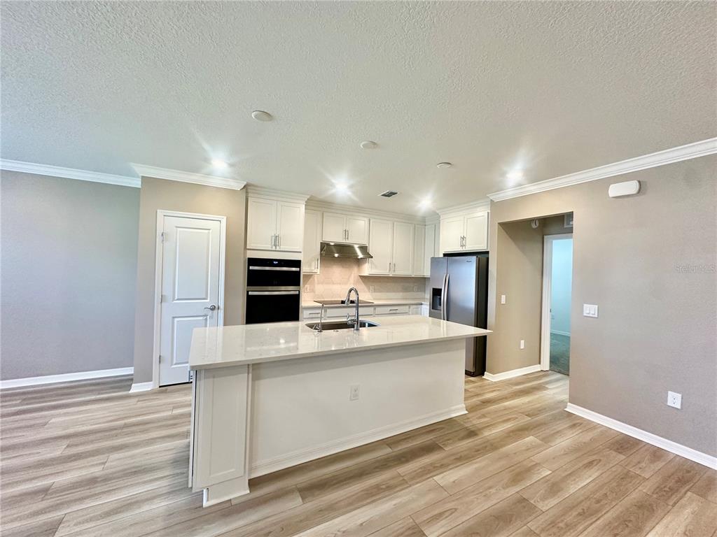 A kitchen features white cabinetry, a central island with a sink, and light wood flooring — 1066 SILVERLAKE BOULEVARD, LAKE ALFRED, FL