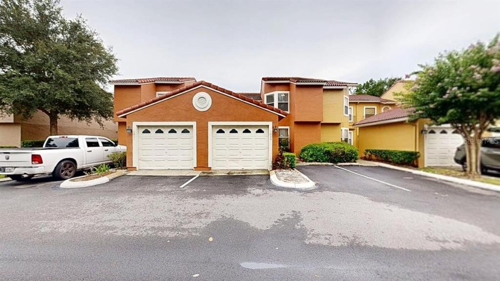 A two-story orange stucco townhouse features two garage doors and a paved parking area — 1009 CASA DEL SOL CIRCLE, ALTAMONTE SPRINGS, FL