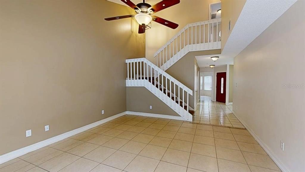 A living room with tile flooring, a high ceiling, and a staircase with white railings — 1009 CASA DEL SOL CIRCLE, ALTAMONTE SPRINGS, FL