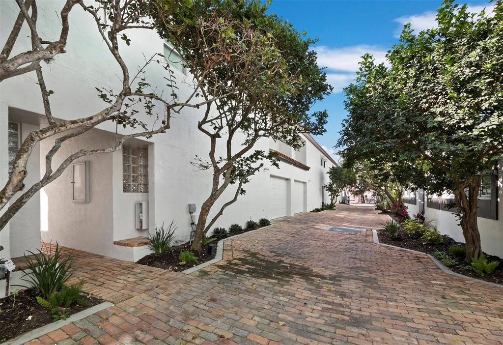A brick driveway leads between white buildings with trees and landscaping on a sunny day — 200 COCOANUT AVENUE UNIT 7, SARASOTA, FL