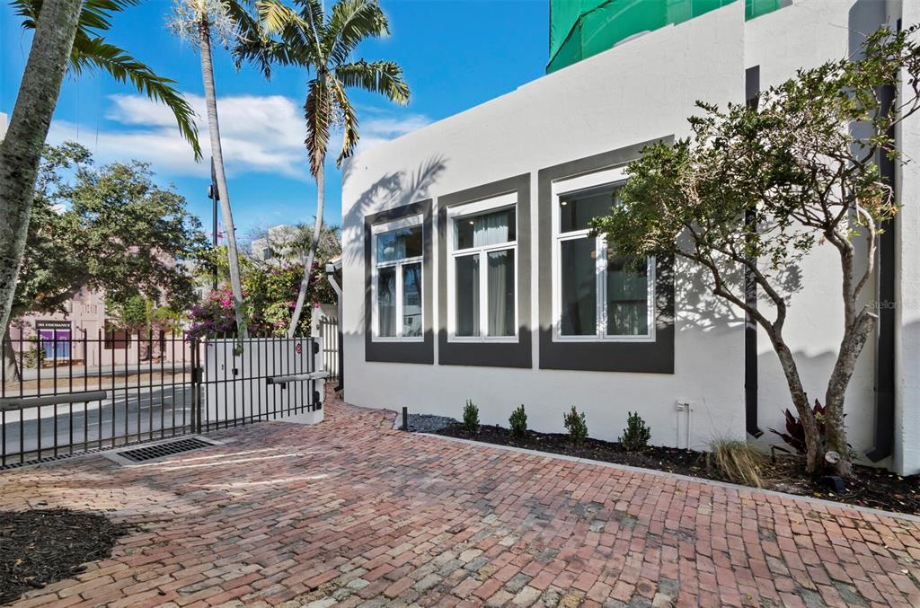 A white building exterior features three windows with dark frames above a brick driveway — 200 COCOANUT AVENUE UNIT 7, SARASOTA, FL