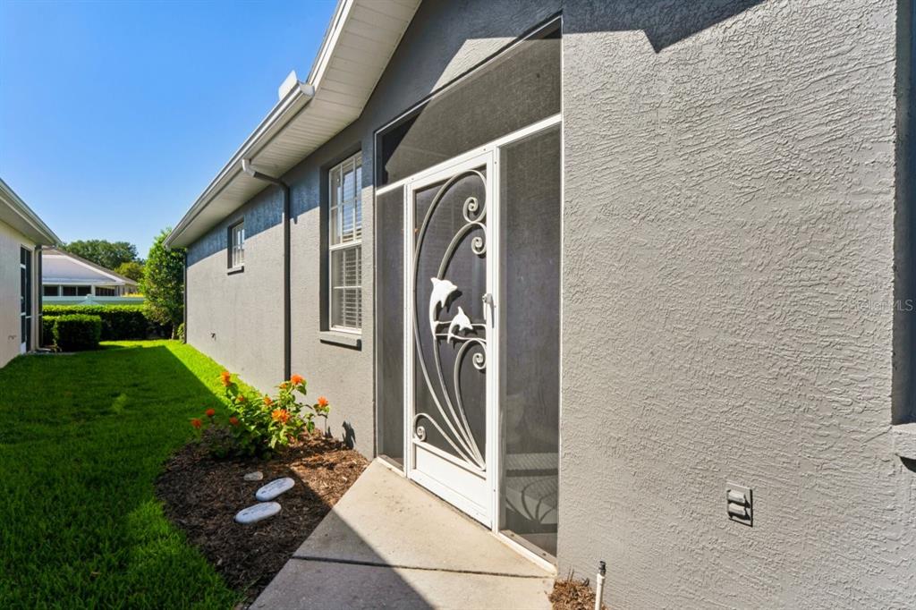 A side view of a gray stucco house with a white dolphin-themed screen door — 14468 MIDDLE FAIRWAY DRIVE, SPRING HILL, FL