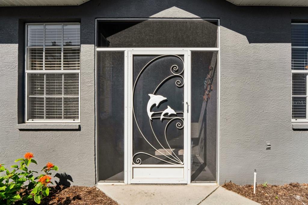 A gray exterior wall features a white screen door with a decorative dolphin metal design — 14468 MIDDLE FAIRWAY DRIVE, SPRING HILL, FL