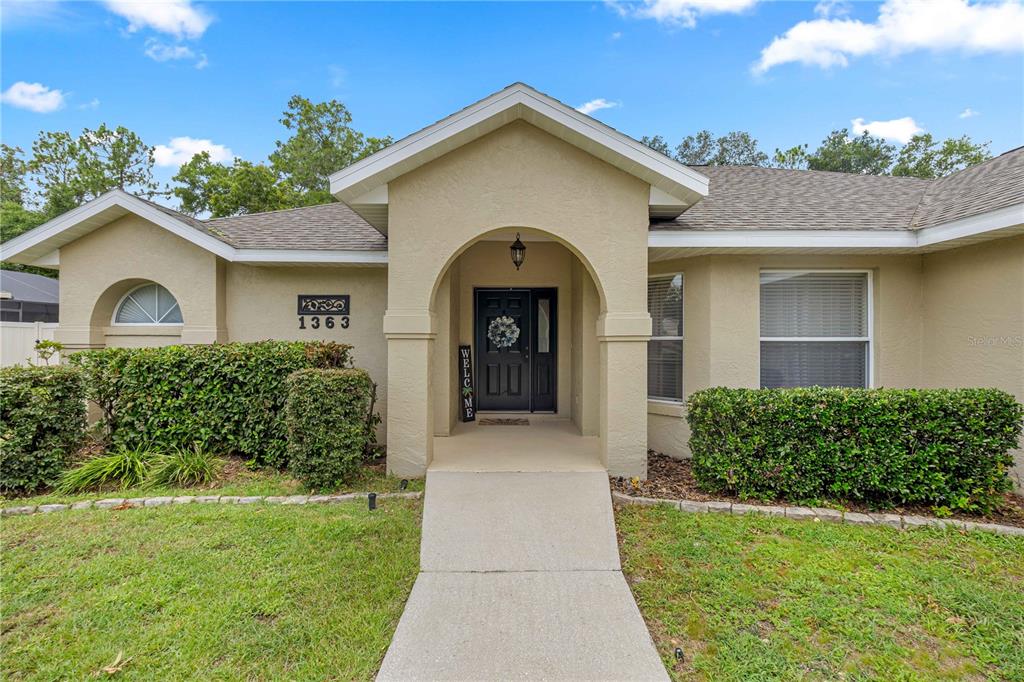 A tan stucco house features an arched entryway, a concrete walkway, and manicured landscaping — 1363 SE 65TH CIRCLE, OCALA, FL
