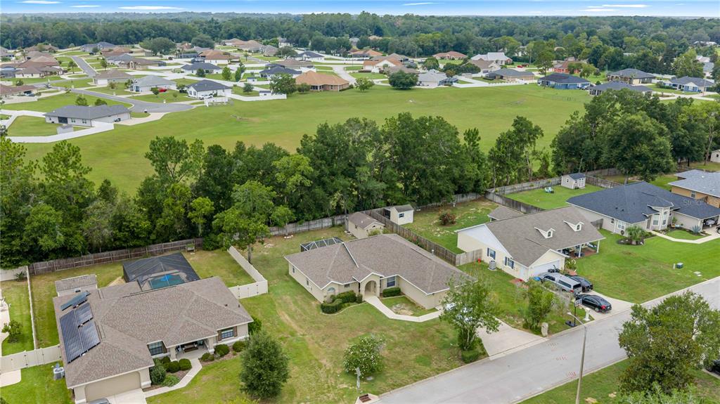 An aerial view shows several suburban houses with fenced yards and a large grassy field — 1363 SE 65TH CIRCLE, OCALA, FL