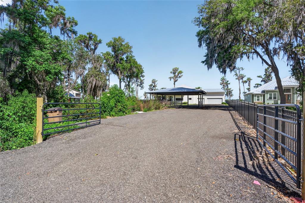 A gravel driveway leads through a metal gate toward a covered structure and house — 2473 SE 30TH STREET, MELROSE, FL