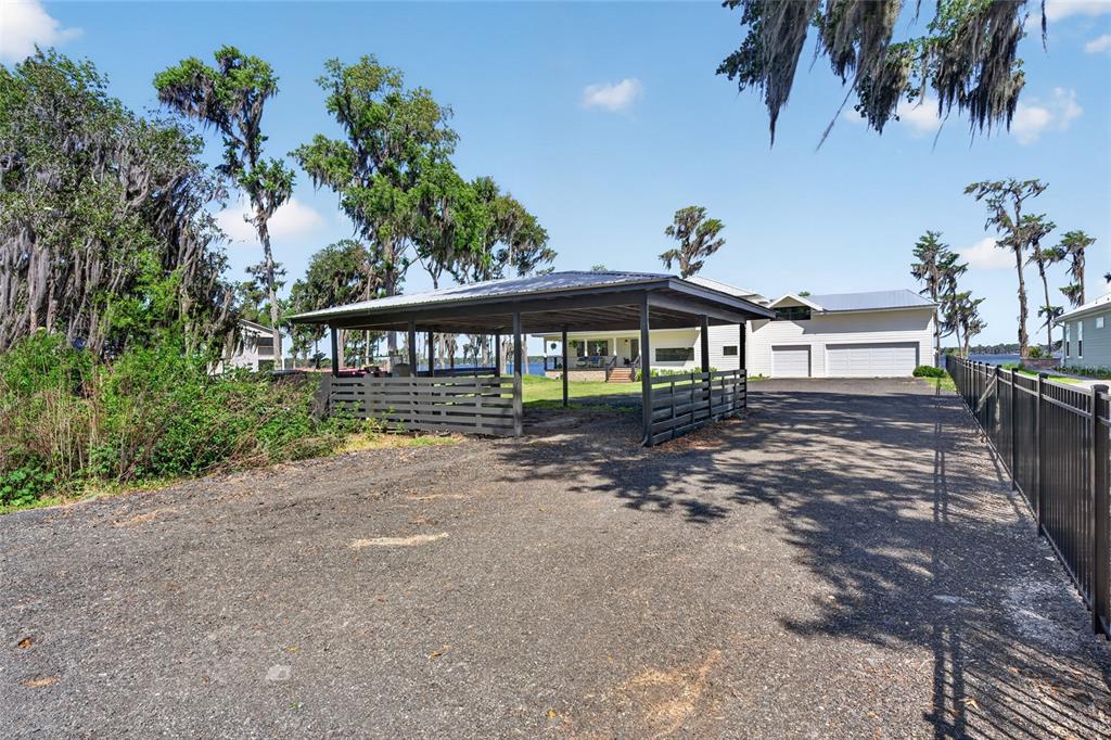 A gravel driveway leads to a covered carport with a dark fence on a sunny day — 2473 SE 30TH STREET, MELROSE, FL