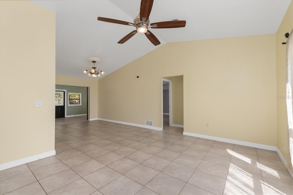 A living room with light yellow walls, tile flooring, a ceiling fan, and vaulted ceilings — 10033 STONECROP AVENUE, ENGLEWOOD, FL