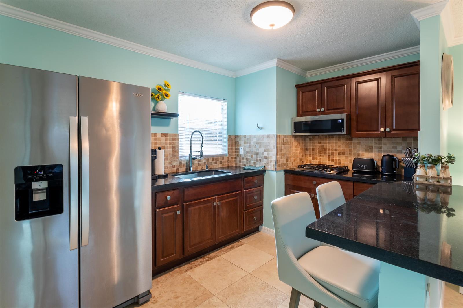 A kitchen with light blue walls, dark wood cabinets, black countertops, and stainless steel appliances — 1724 37th Street, West Palm Beach FL 33407, WEST PALM BEACH, FL
