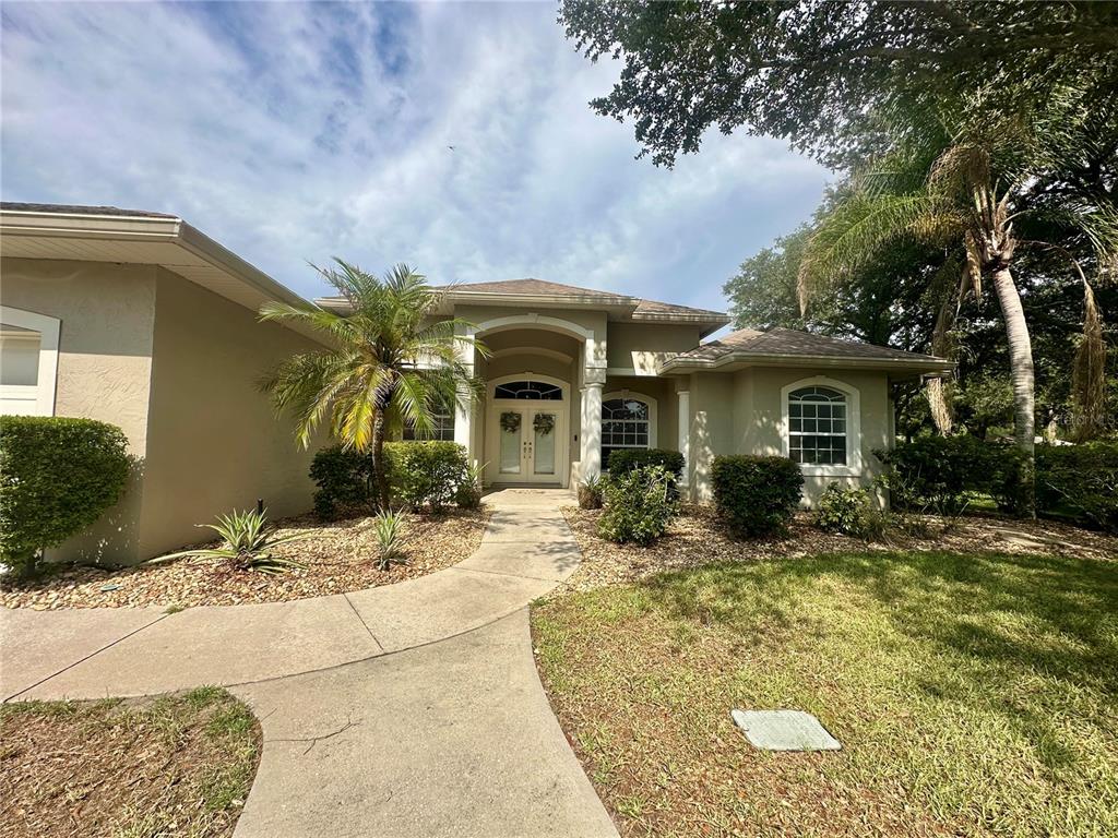 A single-story house with a beige stucco exterior, arched entryway, and a concrete walkway — 1801 SANDHILL LANE, WINTER HAVEN, FL
