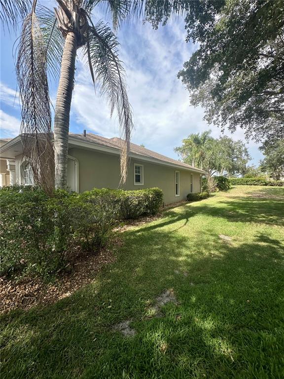 A side view of a beige house with a palm tree and landscaped bushes — 1801 SANDHILL LANE, WINTER HAVEN, FL