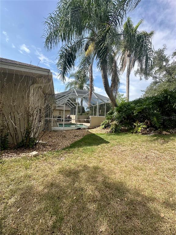 A backyard features a screened-in pool enclosure, palm trees, and a tan house exterior — 1801 SANDHILL LANE, WINTER HAVEN, FL